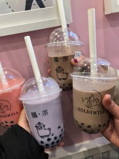 three bubble teas are being held up in front of a pink wall with writing on it