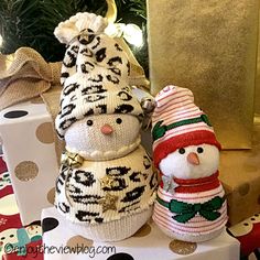 two knitted snowmen sitting next to each other in front of christmas presents on a table