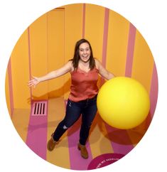 a woman standing in front of a yellow ball and pink striped wall with her arms outstretched