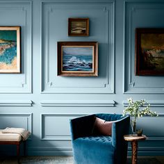 a blue chair in front of a wall with pictures on it and a vase filled with flowers