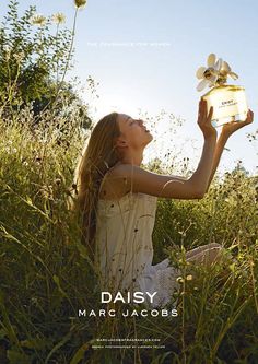 a woman sitting in the grass holding up a box with a flower on top of it