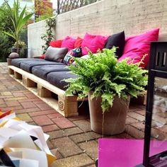 an outdoor seating area with pink and black pillows on the couches, potted plants