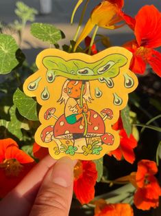 a person holding up a sticker in front of some flowers