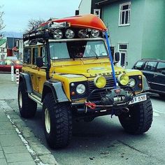 a yellow jeep with an orange surfboard strapped to the top is parked in front of a building