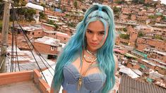 a woman with blue hair standing on top of a roof in front of a city