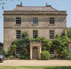 an old stone house with ivy growing on it's walls and windows, in front of a gravel driveway