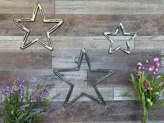 three metal stars on a wooden wall with flowers in vases next to one another