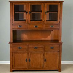 a wooden china cabinet with glass doors on the top and bottom shelf, in front of a gray wall