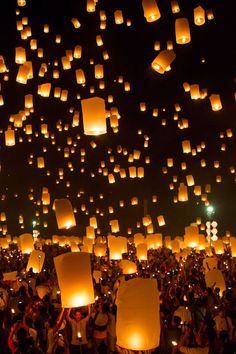 many people are flying lanterns in the sky at night time with bright lights on them