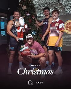 a group of men standing next to each other in front of a christmas tree with santa clause on it