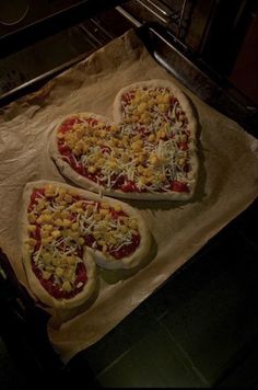 two heart shaped pizzas sitting on top of a baking sheet