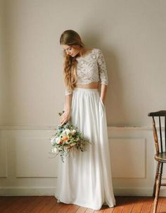 a woman standing in front of a white wall holding a bouquet and wearing a wedding dress