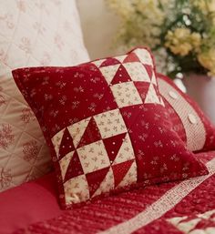 a bed with red and white quilted bedspread, pillows and vase filled with flowers