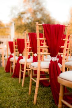 rows of wooden chairs with red sashes and bows on them, lined up in the grass