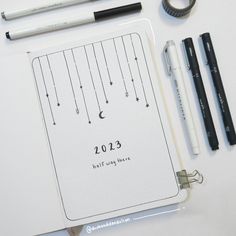 an open notebook with writing on it next to some pens and pencils in front of it