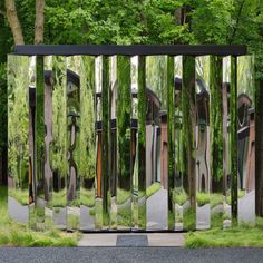 a large metal sculpture sitting in the middle of a park next to a tree filled forest