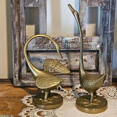 two brass swan figurines sitting on top of a doily