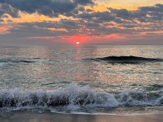 the sun is setting over the ocean with waves crashing on the shore and clouds in the sky