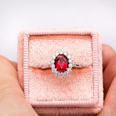 a close up of a person's hand holding a ring with a red stone