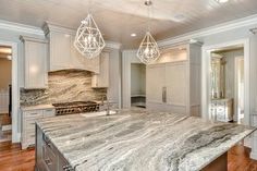 a large kitchen with marble counter tops and white cabinets, along with an island in the middle