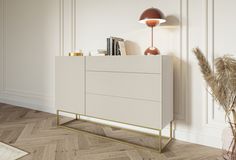 a white cabinet sitting on top of a wooden floor next to a vase and lamp