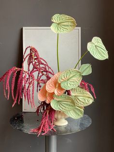 a vase filled with pink and green flowers on top of a metal table next to a mirror