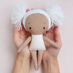 a hand holding a small doll with white hair on it's head and hands