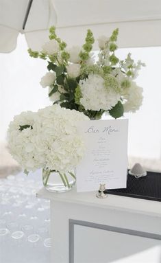 a vase filled with white flowers sitting on top of a table next to a card