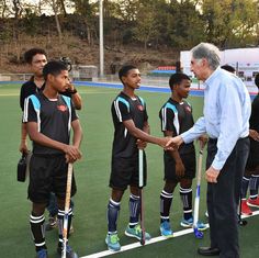 an older man shaking hands with young boys on the field at a hockey game,