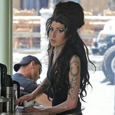 a woman with long hair and tattoos standing at a counter in a restaurant next to a man