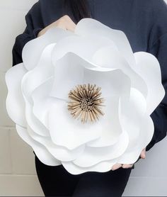 a woman holding a large white paper flower in her hands with the center surrounded by smaller flowers