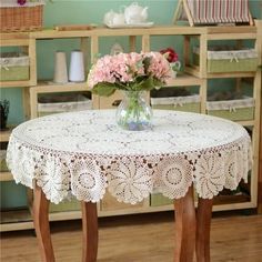 a vase with pink flowers sitting on top of a table in front of some shelves