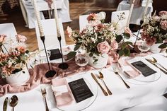 the table is set with white and pink flowers in vases, silverware, and napkins