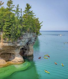 several kayakers are floating in the water near some cliffs and trees on the shore