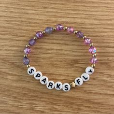 a beaded bracelet with the words sparkle spelled in white letters and beads on a wooden surface