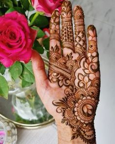 a woman's hand with henna on it and flowers in the vase behind her