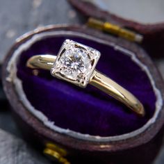 an engagement ring with a diamond in it sitting on top of a purple velvet box