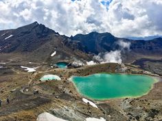 some people are standing on the top of a mountain with green lakes in front of them