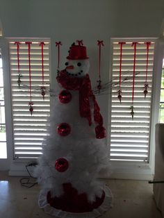 a white christmas tree with red ornaments and a snowman decoration on it's top