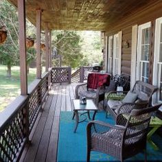 a porch with wicker chairs and tables on the front porch, covered in wood planks