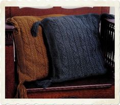 two knitted pillows sitting on top of a wooden bench