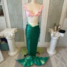 a green and pink mermaid costume on display in front of two white pedestaled tables