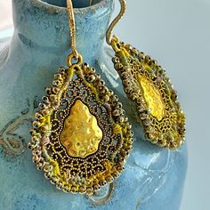 These eye-catching drop earrings feature ornate, antique gold-plated teardrops - with a hammered metal center and a scrolling filigree border. I embellished the edges with crochet using hand-dyed, cotton thread in shades of golden yellow, sage green, and taupe and tiny, faceted, metallic gold glass beads.  These earrings shimmer with reflected light.  They are finished with half-hammered, gold-plated brass (nickel and lead free) ear wires.  These earrings hang to a length of 2 1/4 inches.  The drops are 1 1/2 inches long and about 1 1/8 inches wide.  One of a kind beauties! Antique Gold Chandelier Earrings In Brass, Antique Gold Metal Chandelier Earrings, Antique Gold Teardrop Earrings, Gold Beaded Earrings For Pierced Ears, Antique Teardrop Brass Earrings, Vintage Brass Earrings For Celebrations, Artisan Gold Beaded Earrings, Ornate Brass Earrings For Celebration, Nickel-free Gold Beaded Metal Earrings