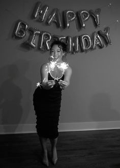 a woman holding sparklers in front of a happy birthday sign