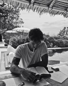 a man sitting at a table with an open book in front of him, reading