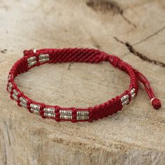 a red string bracelet with silver beads on top of a piece of driftwood trunk