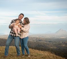 a man and woman holding a baby on top of a hill