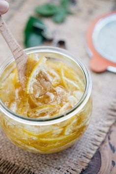 a person holding a wooden spoon in a jar filled with lemon and ginger syrup on a table