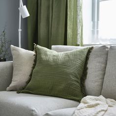 a white couch with green pillows and a blanket on it's back in front of a window