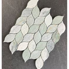 a white and gray mosaic tile with leaves on the bottom, sitting on a black surface